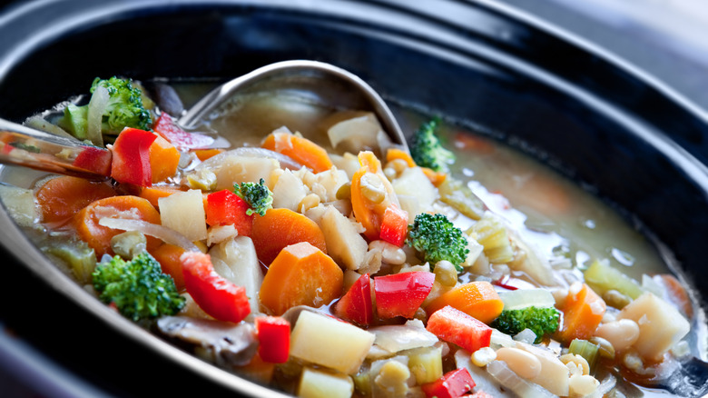 Close up of ladle with various vegetables in slow cooker
