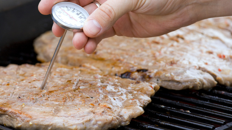 Person checking meat temperature while grilling