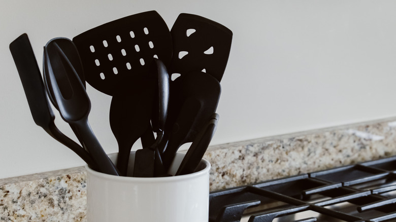 Black cooking utensils in a white container on a kitchen counter