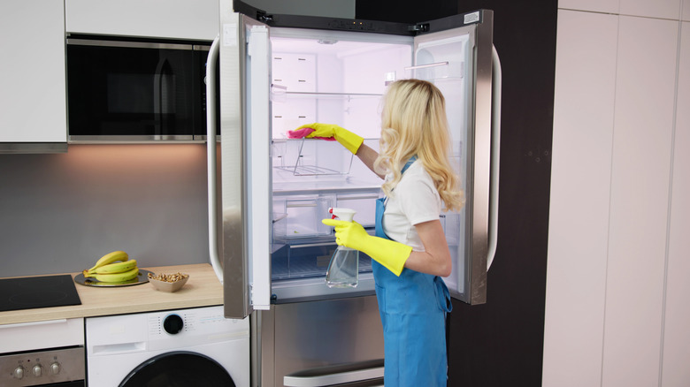 A young woman wearing rubber gloves cleans a refrigerator