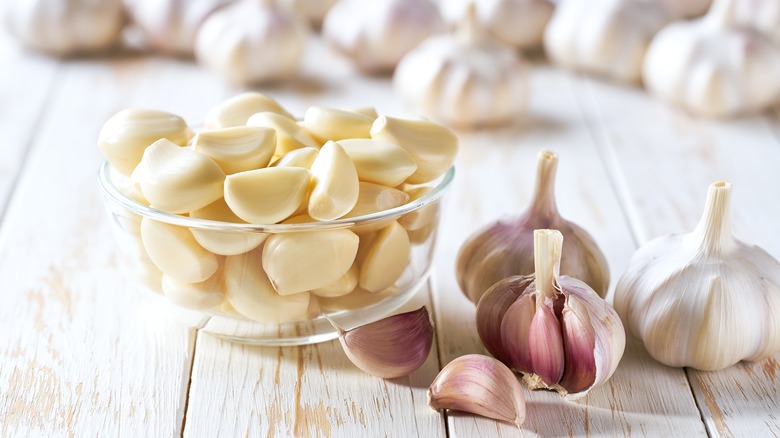 Fresh garlic cloves in a bowl with whole garlic on the side on a white wooden table