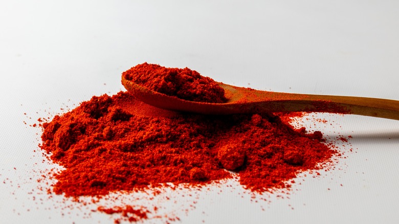 A heap of paprika on a wooden spoon against a white background