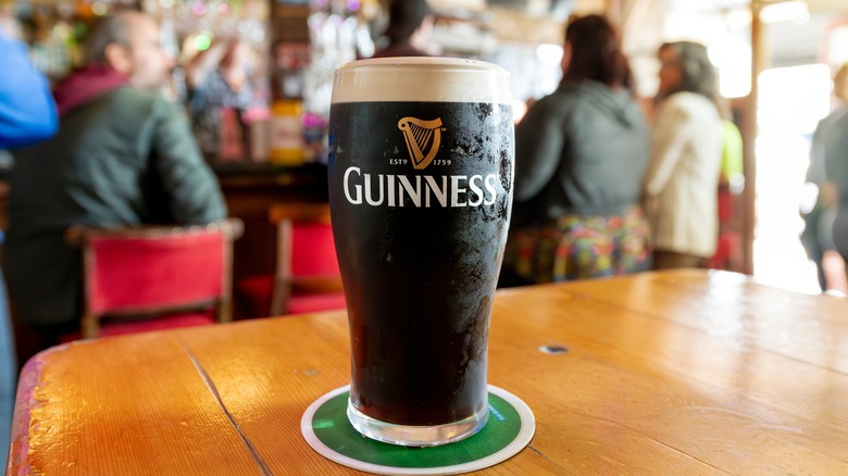 Cold glass of Guinness on a table with a blurred bar and patrons in the background