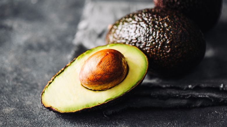 Avocado half and two whole avacados on black slate