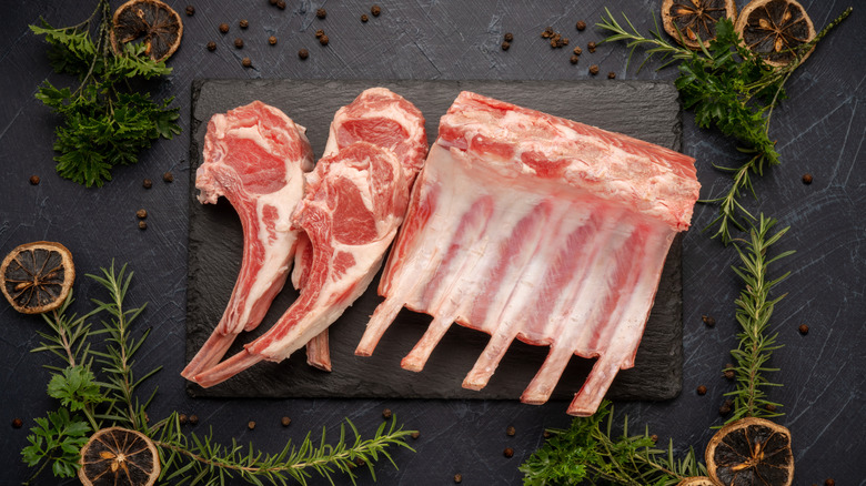 Raw lamb chops cut from a rack of lamb on a dark background with fresh rosemary