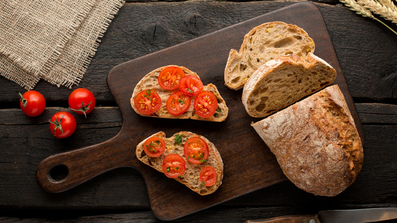 Open-face tomato sandwich on wooden cutting board with loaf of rustic bread and knife