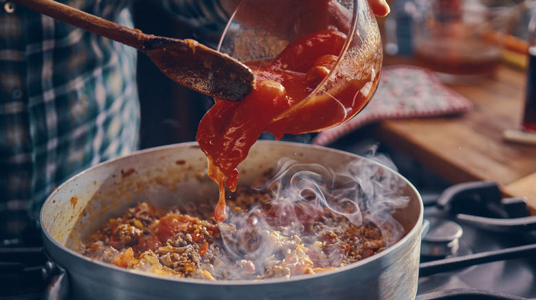 Person adding tomatoes to meat sauce