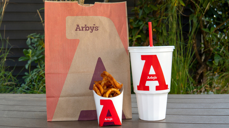 Arby's bag, carton of french fries, and plastic drink cup with straw on table outdoors