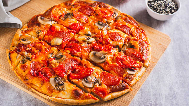Round, square-cut pizza with mushrooms and pepperoni on a wooden board atop a gray background